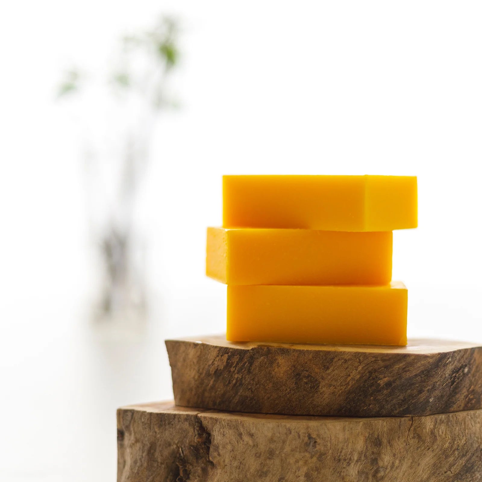 Three yellow soap bars stacked on a wooden surface with a blurred natural background