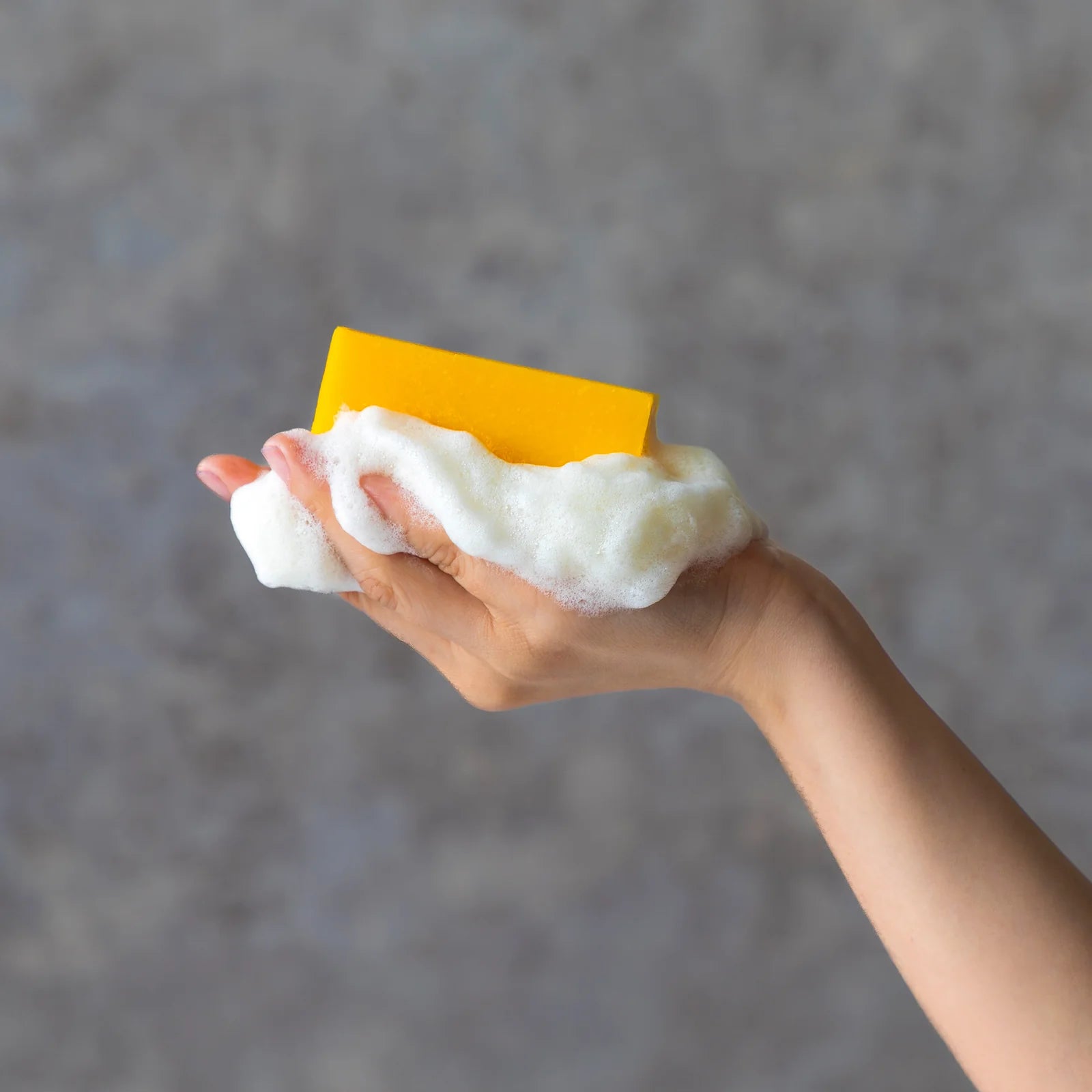 Hand holding a yellow soap with white foam against a gray background